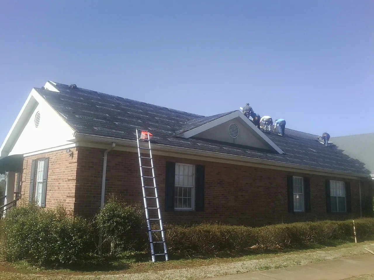 Crew tearing shingles off a brick ranch roof with a ladder set — Metal Roof Repair work by our crew in Lawrence Township