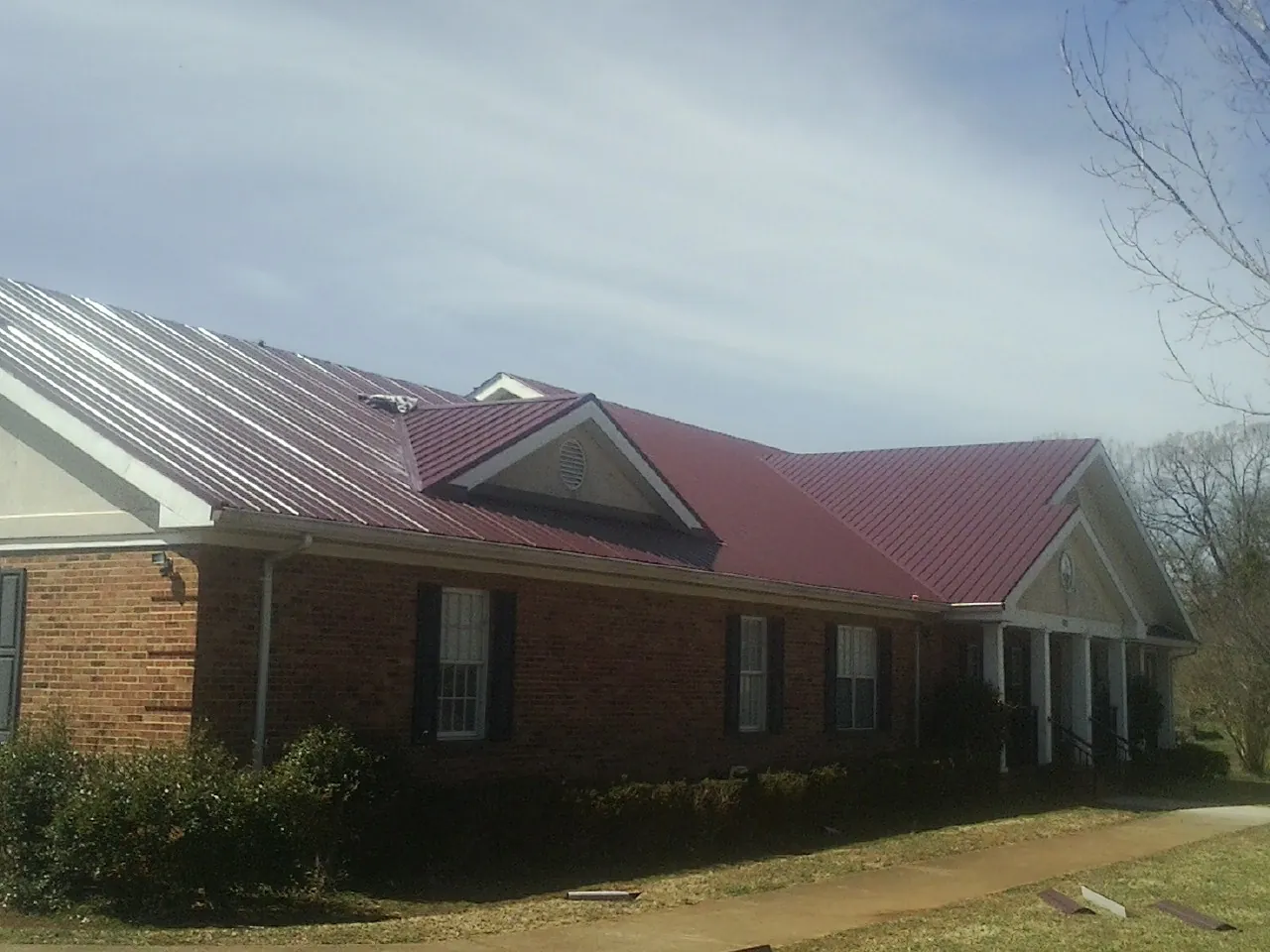 Red metal roof with gabled entries on a long brick building, from a Hail Damage Roof Repair job in Lawrence Township
