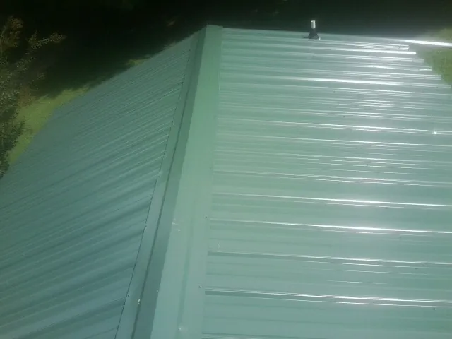 New green metal panels meeting at the ridge of a roof — Flat Roof Repair work by our crew in Lawrence Township