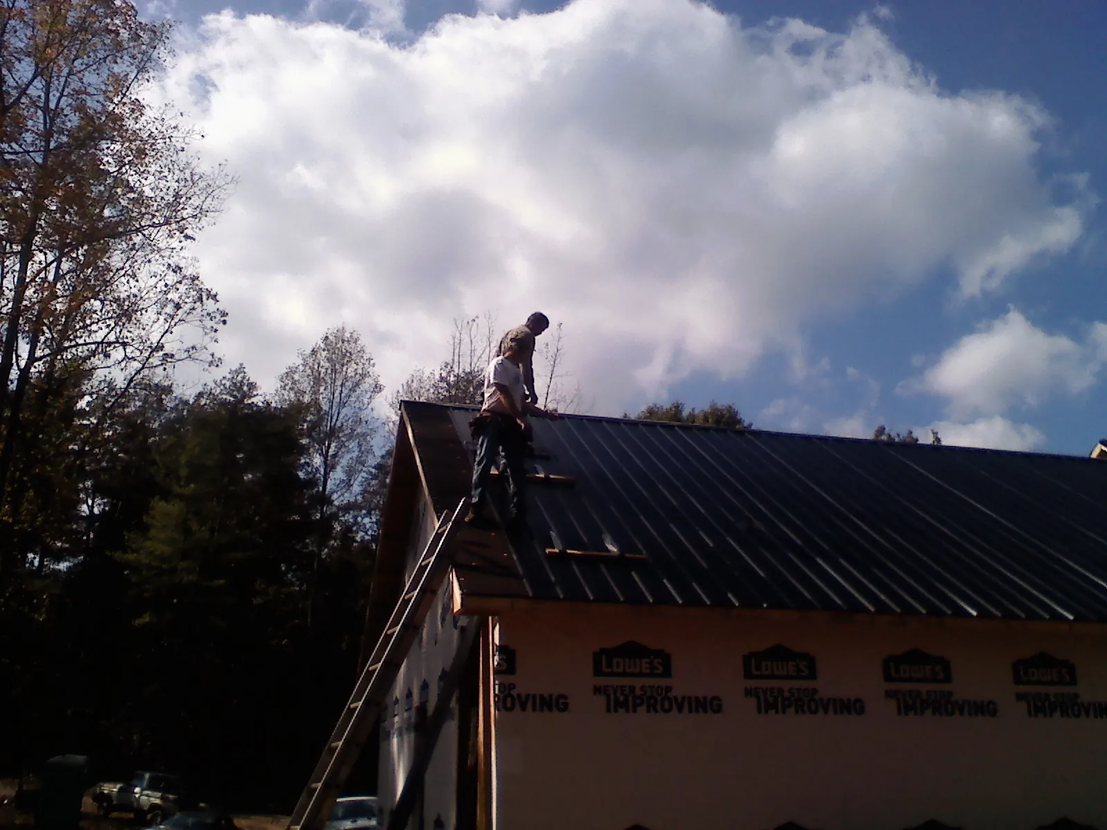 Roofer fastening dark metal panels high against a cloudy sky, from a Roof Inspection job in Lawrence Township