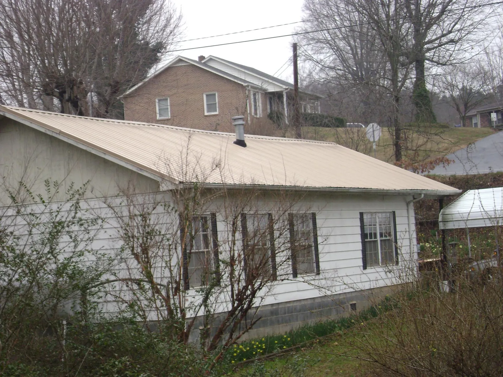 Tan metal roof on a white sided house set into a hillside — Commercial Roofing by Roofing Brothers in Lawrence Township